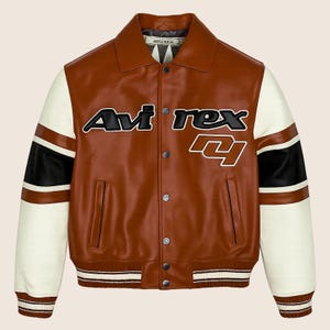 May include: Brown leather jacket with white and black accents on the sleeves. The jacket features the text "Avirex" in black and white lettering on the chest. The jacket has a ribbed collar, cuffs, and hem.