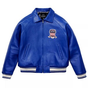 May include: A vibrant blue leather jacket with a classic collar and a zip-up front. The jacket features a white and blue striped trim on the cuffs and hem. An embroidered patch with the text "AVIREX" and a patriotic design is on the chest.