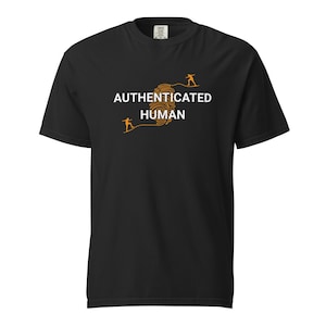 以下が含まれることがあります： 「AUTHENTICATED HUMAN」の白い文字とオレンジ色の指紋デザインが特徴の黒いTシャツ。指紋の両側に2つのオレンジ色の人物が描かれています。このシャツは柔らかい素材で作られています。