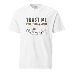 May include: White t-shirt with the text "TRUST ME I WATCHED A VIDEO" in green and brown. Below the text are stick figure illustrations of a person, a broken house, and people climbing a wall.