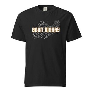 Peut inclure: T-shirt noir avec l'inscription "BORN BINARY" en orange et blanc. Le motif comprend une vague de code binaire blanc. Le t-shirt est à col rond et à manches courtes.