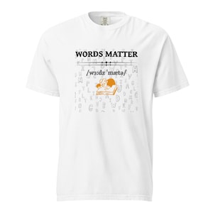 May include: White t-shirt with the text "WORDS MATTER" above a graphic of a person reading a book. The graphic is in orange and black. The shirt also has the phonetic spelling of "words matter".