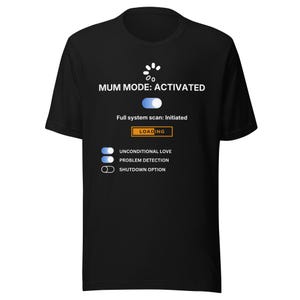 Puede incluir: Camiseta negra con el texto "MUM MODE: ACTIVATED" y un gráfico que se asemeja a una pantalla de carga. La camiseta incluye opciones para el amor incondicional, la detección de problemas y una opción de apagado.