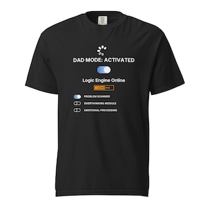 Op de afbeelding: Zwart t-shirt met de tekst "DAD MODE: ACTIVATED" en een afbeelding die lijkt op een laadscherm. Het ontwerp bevat "Logic Engine Online" en opties voor "Problem Scanner", "Overthinking Module" en "Emotional Processing".