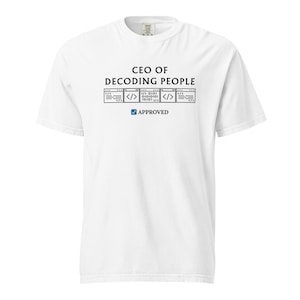 May include: White t-shirt featuring the text "CEO OF DECODING PEOPLE" above a graphic of code and the word "APPROVED" with a tick. The shirt has short sleeves and a crew neck.