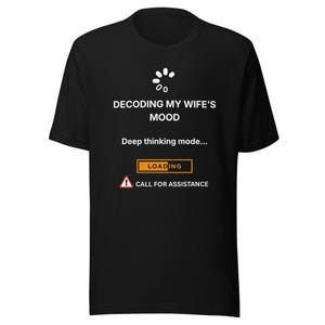 Könnte beinhalten: Schwarzes T-Shirt mit weißem Text: "DECODING MY WIFE'S MOOD", "Deep thinking mode..." und eine "LOADING" Leiste. Darunter ein Warnschild mit "CALL FOR ASSISTANCE". Das T-Shirt hat einen Rundhalsausschnitt und kurze Ärmel.