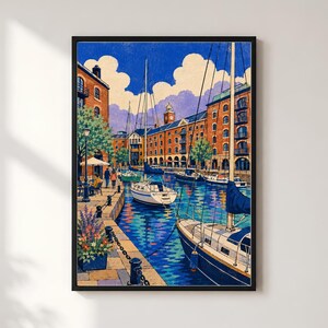 May include: A framed art print depicting a canal scene with sailboats moored in blue water. Red brick buildings line the waterfront, featuring arched windows and balconies. A paved walkway with a lamppost, potted flowers, and people is visible.