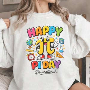 Pode incluir: Camisola branca com um gráfico colorido que celebra o Dia do Pi. O design apresenta as palavras "HAPPY PI DAY" e "Be irrational" com um símbolo pi de desenho animado e ícones relacionados com a matemática. O símbolo pi usa sapatos vermelhos.
