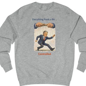 May include: A heather gray sweatshirt with a graphic of a man in a suit being controlled by puppet strings. The text "Everything Feels a Bit..." and "Controlled" are printed on the sweatshirt.