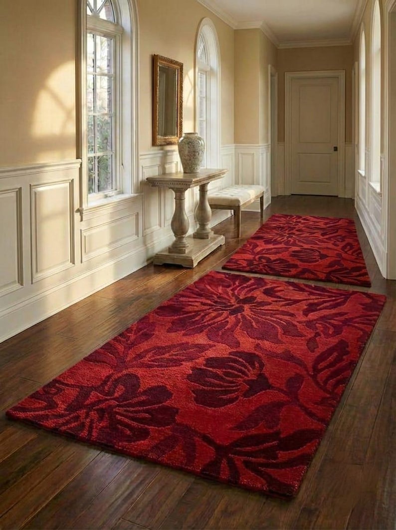 Puede incluir: Dos alfombras rojas con estampado floral sobre un suelo de madera noble en un pasillo. Las alfombras tienen un dise&ntilde;o floral rojo oscuro sobre un fondo rojo m&aacute;s claro. El pasillo tiene paredes color crema y molduras blancas.