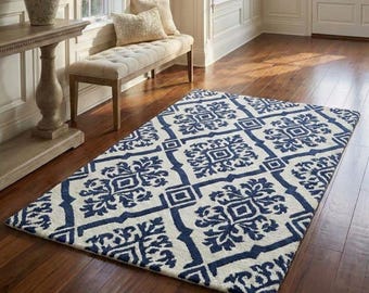 Puede incluir: Una alfombra rectangular con un fondo color crema y un patrón geométrico azul marino repetido. La alfombra está colocada sobre un suelo de madera en una habitación bien iluminada, mostrando su diseño decorativo.