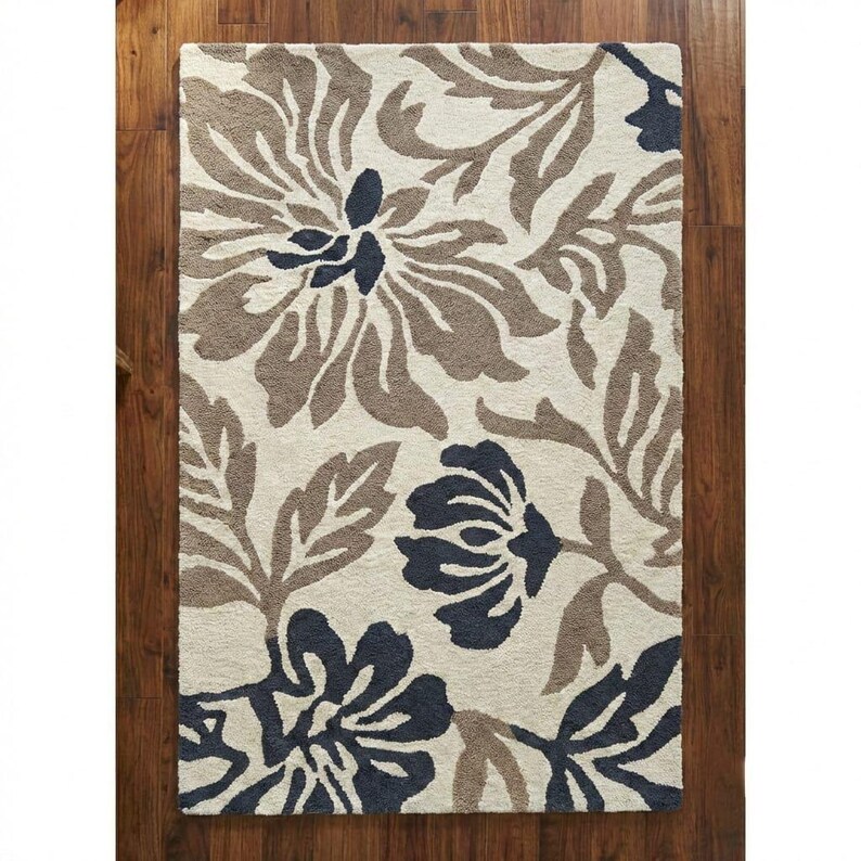 Puede incluir: Una alfombra rectangular con un dise&ntilde;o floral. La alfombra presenta grandes flores estilizadas en tonos marr&oacute;n y azul marino sobre un fondo crema. La alfombra est&aacute; colocada sobre un suelo de madera.