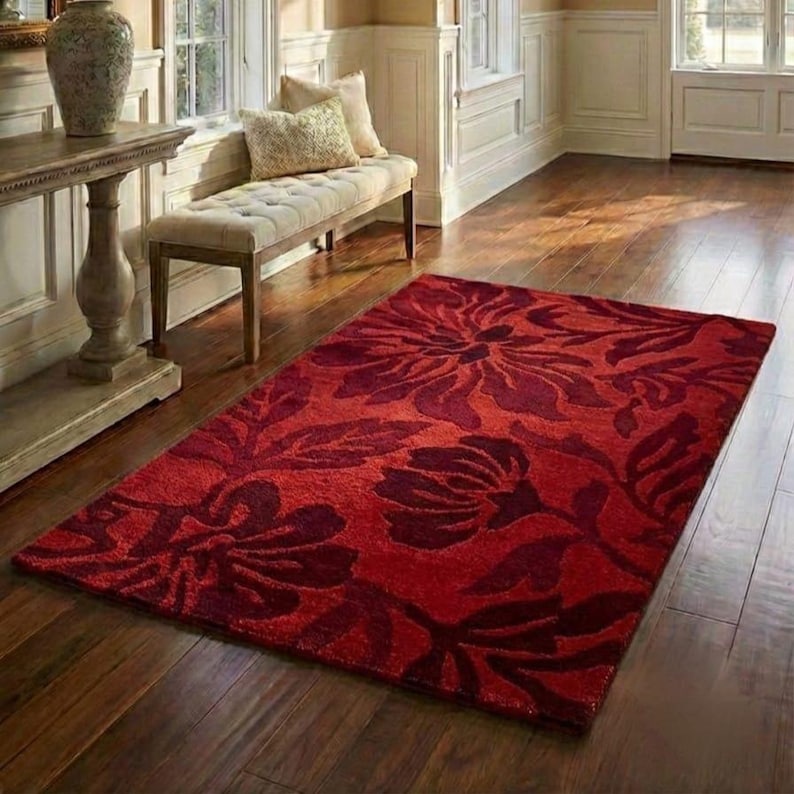 Puede incluir: Una alfombra rectangular roja con un estampado floral en diferentes tonos de rojo. La alfombra est&aacute; colocada sobre un suelo de madera y el dise&ntilde;o floral es prominente. La alfombra a&ntilde;ade un elemento decorativo a la habitaci&oacute;n.