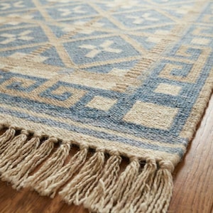 Könnte beinhalten: Rechteckiger Teppich mit geometrischem Muster in Blau- und Beigetönen. Der Teppich hat ein sich wiederholendes Design aus Quadraten und Rauten. Der Rand des Teppichs hat eine Fransenverzierung. Der Teppich besteht aus einem gewebten Material.
