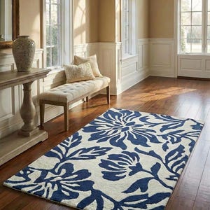 Puede incluir: Una alfombra rectangular con un dise&ntilde;o floral en azul marino y crema. La alfombra est&aacute; colocada sobre un suelo de madera en una habitaci&oacute;n con luz natural y un banco. El patr&oacute;n de la alfombra presenta grandes flores y hojas estilizadas.