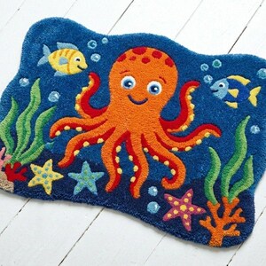 May include: A blue, ocean-themed rug with an orange octopus, yellow and blue fish, green seaweed, and colorful starfish. The rug is shaped like a wavy rectangle and is designed for a child's room or playroom.