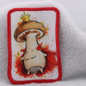 Op de afbeelding: Rechthoekige patch met een cartoon paddenstoel koning ontwerp. De paddenstoel draagt een gouden kroon en rode cape, met een scepter. De patch heeft een rode rand en is geplaatst tegen een witte achtergrond.