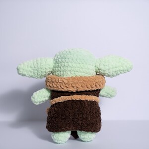 Puede incluir: Mu&ntilde;eca de ganchillo hecha a mano a semejanza de un personaje popular. La mu&ntilde;eca presenta una cabeza y orejas de color verde claro, una t&uacute;nica marr&oacute;n y un cuello color canela. La mu&ntilde;eca est&aacute; hecha de hilo suave y texturizado.