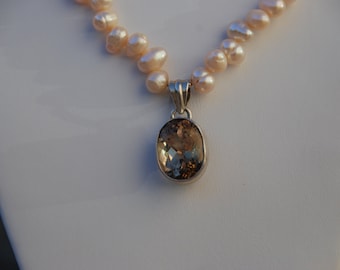 May include: A delicate pearl necklace with a brown gemstone pendant. The necklace is made of small, round pearls and the pendant is a large, oval-shaped gemstone.