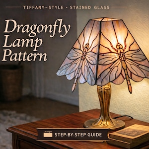 May include: A Tiffany-style stained glass lamp with a dragonfly design. The lamp has a beige and blue lampshade with dragonfly illustrations. The base is gold-coloured, and the lamp is on a wooden table. The text on the image reads "Dragonfly Lamp Pattern".