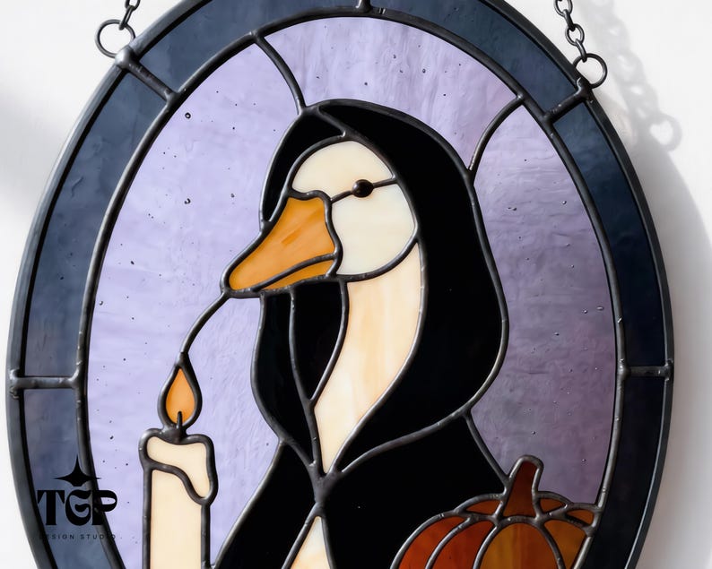 Puede incluir: Vidriera que representa un pato con una capa con capucha negra, sosteniendo una vela con una llama naranja. El pato tiene un pico naranja y est&aacute; sobre un fondo p&uacute;rpura dentro de un marco ovalado negro. Tambi&eacute;n se ve una peque&ntilde;a calabaza.