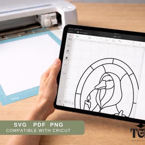 Puede incluir: Un dibujo lineal en blanco y negro de un pato con una vela se muestra en la pantalla de una tableta. La tableta est&aacute; sujeta en las manos de una persona. La imagen est&aacute; junto a una m&aacute;quina Cricut y una esterilla de corte. El texto de la imagen dice: SVG PDF PNG COMPATIBLE CON CRICUT.