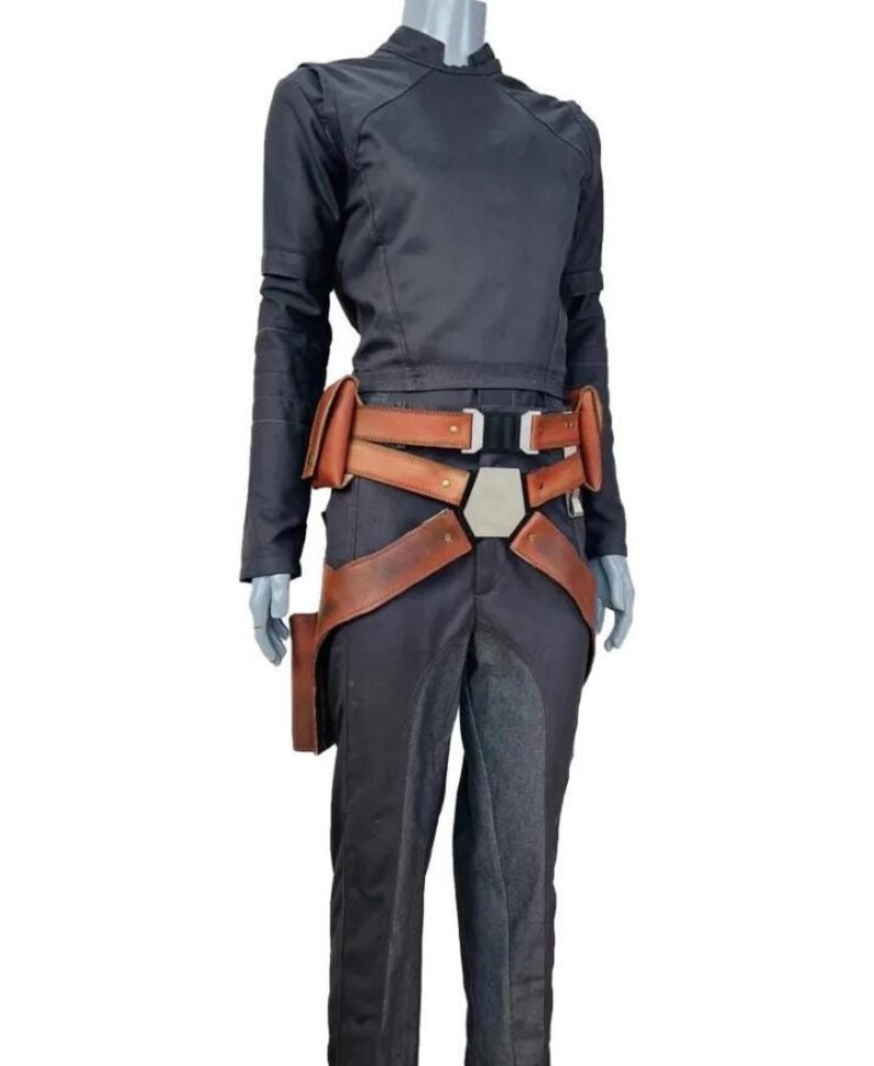 May include: A black long-sleeved shirt and matching black trousers paired with a brown leather utility belt. The belt features multiple pouches, a central metallic hexagonal buckle, and adjustable straps that extend down the hips.