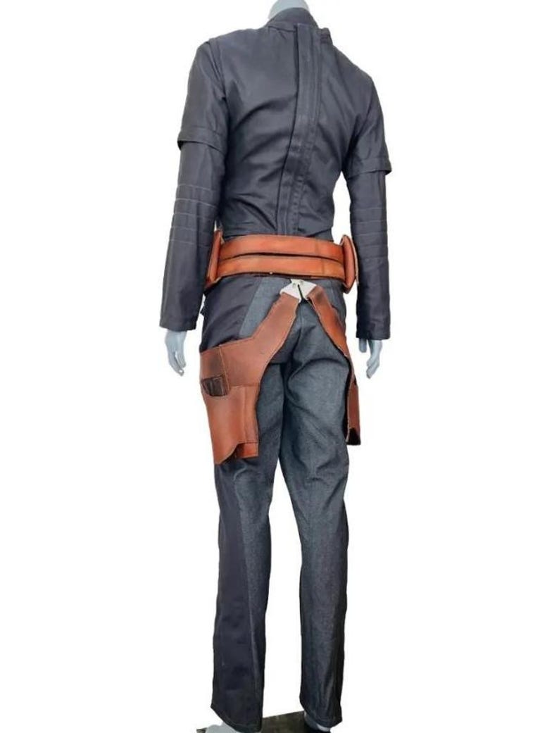 May include: A dark gray long-sleeved jacket and matching trousers paired with a tan leather utility belt. The belt features a prominent holster attachment on the right side, secured with metallic hardware, worn over the dark gray fabric ensemble.