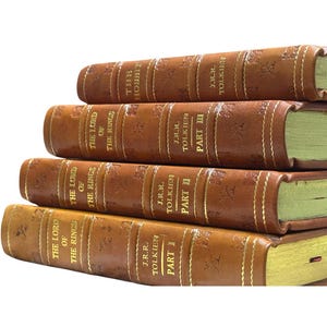 May include: A stack of leather-bound books with gold lettering. The titles include "The Hobbit" and "The Lord of the Rings" by J.R.R. Tolkien. The books are brown with gold-colored page edges.