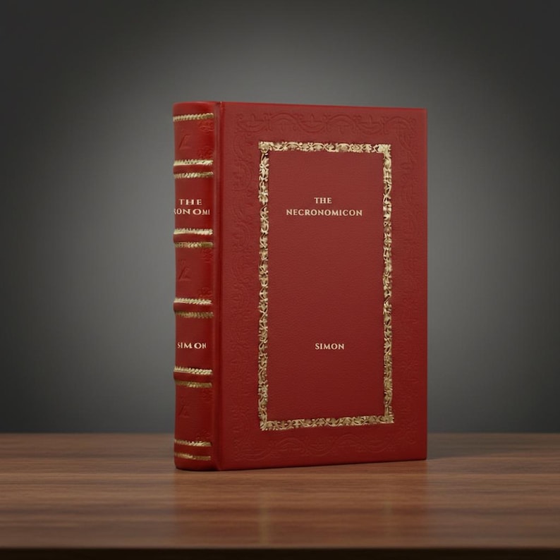 May include: A red hardcover book titled "The Necronomicon" by Simon. The book has gold lettering and decorative gold borders. The spine reads "The Simon Omi". The book is on a wooden surface.