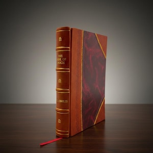 Peut inclure: Un livre à couverture rigide intitulé "The Book of Enoch" avec une couverture en cuir marron et des lettres dorées. Le livre a une section à motifs bordeaux et un signet en ruban rouge. La tranche présente des accents dorés décoratifs.