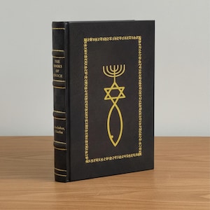 Puede incluir: Un libro de tapa dura negro titulado "The Books of Enoch" con detalles dorados. La portada presenta una estrella de David dorada, un menor&aacute; y un s&iacute;mbolo de pez dentro de un borde decorativo. El lomo muestra el t&iacute;tulo y el nombre del autor.