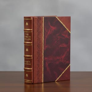 May include: A leather-bound book, "The King in Yellow" by Robert W. Chambers, with a brown cover and gold detailing. The front cover has a burgundy marbled pattern. The spine displays gold lettering and decorative elements.