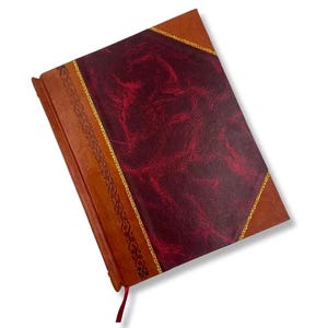 May include: A leather-bound journal with a burgundy cover and brown spine. The cover features a textured pattern and is accented with gold trim. A red ribbon bookmark is attached. The journal is a classic stationery item.