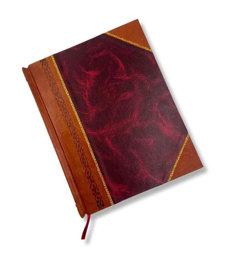 May include: A leather-bound journal with a burgundy cover and brown spine. The cover features a textured pattern and is accented with gold trim. A red ribbon bookmark is attached. The journal is a classic stationery item.