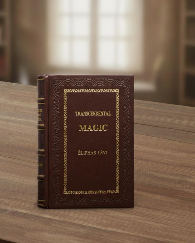 May include: A hardcover book titled "Transcendental Magic" by &Eacute;liphas L&eacute;vi. The book has a dark brown cover with gold lettering and decorative borders. The book is standing upright on a wooden surface.