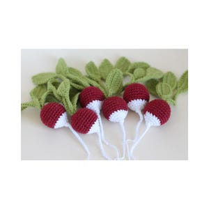 May include: A group of crocheted radishes with green leaves. The radishes are a deep red colour with white bottoms and long white stems. The green leaves are also crocheted, adding a realistic touch to the craft.