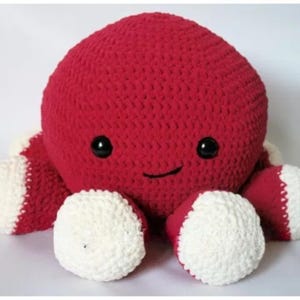 May include: A handmade, red crocheted octopus soft toy with white tentacle tips. The octopus has a smiling face with black eyes. This soft toy is suitable for children and makes a great gift.