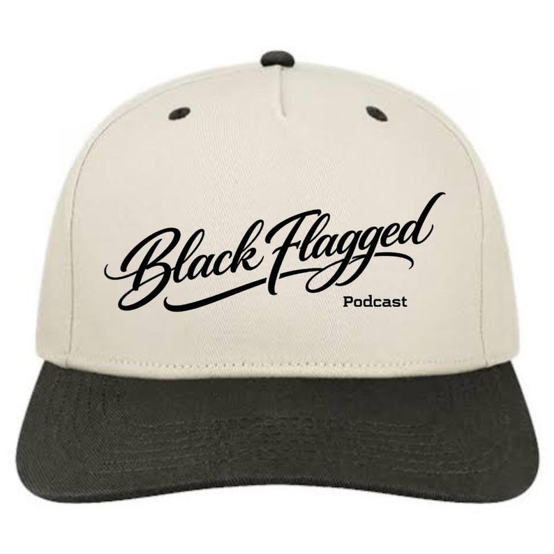 May include: A baseball cap with a cream-coloured crown and a dark grey brim. The cap features the text "Black Flagged Podcast" in a stylish, cursive font. The cap has a classic, structured design.