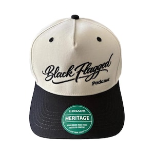 Puede incluir: Gorra de béisbol crema y negra con el texto "Black Flagged Podcast" bordado en negro. La gorra tiene una visera negra y una pegatina "Legacy Heritage" verde y blanca.