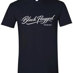 May include: A navy blue t-shirt with the words "Black Flagged" in a white, cursive font, with "Podcast" in a smaller font below. The shirt is a crew neck style.
