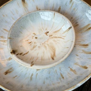 May include: Two ceramic plates, one nested inside the other. The larger plate is light blue with brown streaks, and the smaller plate is white with brown and beige patterns. The plates have a glossy finish.