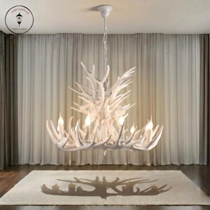 May include: White antler chandelier with multiple light bulbs. The chandelier is suspended from the ceiling and casts a shadow on the rug below. The room has white curtains and a white rug.