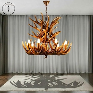 May include: A rustic antler chandelier with six candle-style lights. The fixture is suspended from a bronze-colored chain and ceiling mount. The chandelier's design casts a shadow on the light-colored rug below.