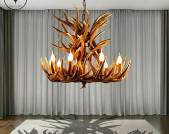 May include: A rustic antler chandelier with six candle-style lights. The fixture is suspended from a bronze-colored chain and ceiling mount. The chandelier's design casts a shadow on the light-colored rug below.