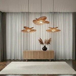 May include: Three light brown, circular, tiered pendant lamps with thin, radiating slats hang from the ceiling. Below them sits a rectangular, light wood slatted sideboard with a black vase containing dried, feathery, brown botanical stems.