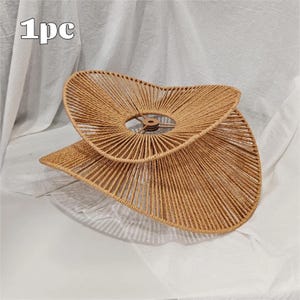 May include: A tan, woven rope lampshade with a wide, asymmetrical, wavy-edged design. The structure features a central circular metal frame with a light brown finish. The text '1pc' is visible in the upper left corner of the image.