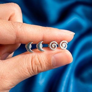 Op de afbeelding: Een set van vier zilverkleurige oorstekers. Er zijn twee paar oorbellen zichtbaar: halve maanvormen en spiraalontwerpen. De oorbellen zijn klein en delicaat, geschikt voor dagelijks gebruik.
