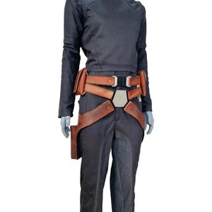 Pu&ograve; includere: Una maglia nera a maniche lunghe e pantaloni neri abbinati, completati da una cintura multiuso in pelle marrone. La cintura presenta diverse tasche, una fibbia centrale esagonale in metallo e cinghie regolabili sui fianchi.