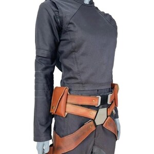 Pu&ograve; includere: Una maglia a maniche lunghe grigio scuro con collo alto e pantaloni abbinati, abbinata a una cintura multiuso in pelle color cuoio con diverse tasche, una fibbia centrale esagonale in metallo e cinghie integrate per le gambe con finiture in ottone.